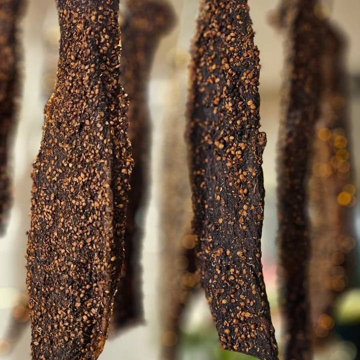 Dried strips of meat hanging, coated in spices and dark in colour.
