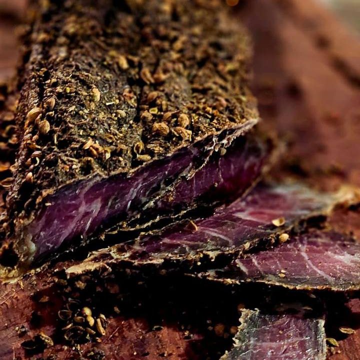 Sliced cured meat coated in spices on a wooden surface.